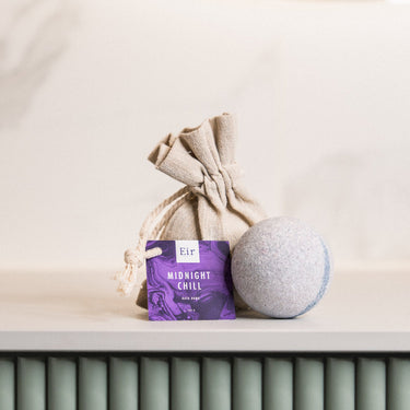 Packaging of Eir's 'Midnight Chill' bath bomb, a jute pouch, and a grey bath bomb on a radiator in a bright interior.