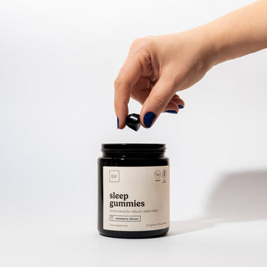 Hand with navy blue nail polish opening a black jar of Eir Health natural sleep gummies. Minimalist white label shows product information and vegan certification on white background.