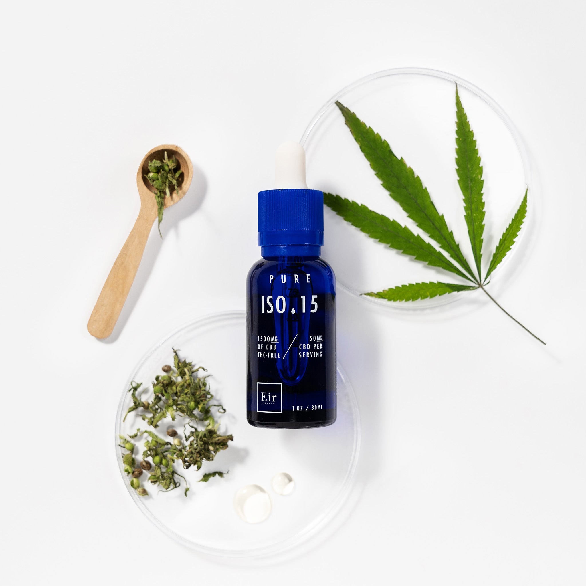Bottle of CBD oil ISO 15 against a background of green cannabis leaves and a wooden spoon with dried herbs.