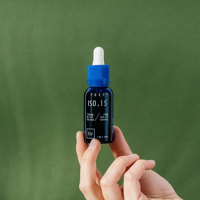 Bottle of CBD oil ISO 15 on a green background, held between fingers.